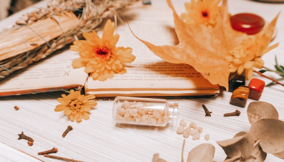 orange flower on white book page with Frankincense in a mini glass bottle with cloves and dried flowers surrounding.