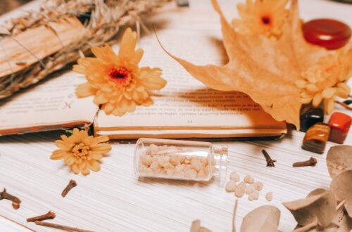 orange flower on white book page with Frankincense in a mini glass bottle with cloves and dried flowers surrounding.