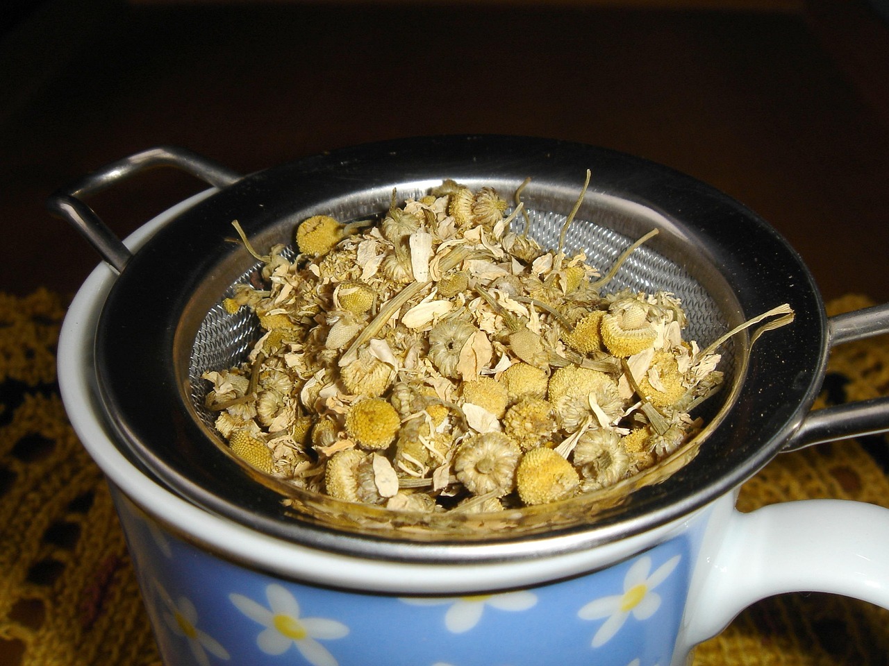 Dried Chamomile in a strainer above a teacup.